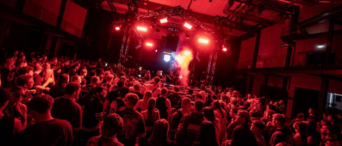 Blick über die gesamte Halle: Crowd rund um die zentrale Stage im roten Licht